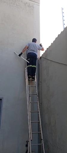 Técnico em escada instalando cerca elétrica no muro do corredor lateral