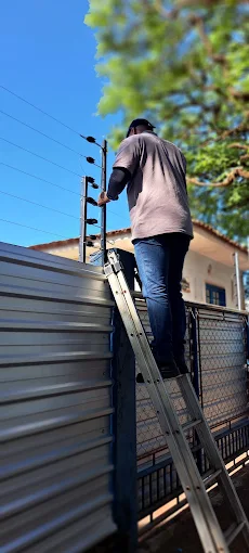 Técnico em escada instalando cerca elétrica sobre o portão frontal de uma casa