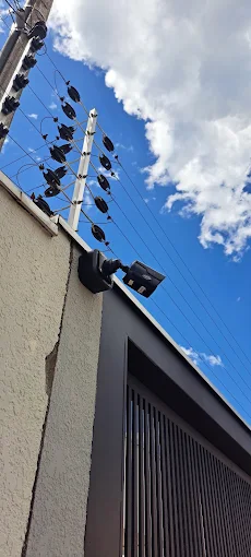 Cerca elétrica e refletor instalados no alto do muro, ao lado do portão