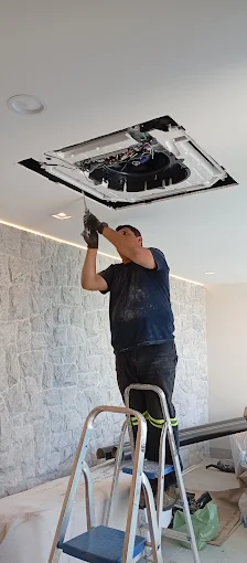 Técnico fazendo a manutenção de um ar-condicionado cassete instalado no teto