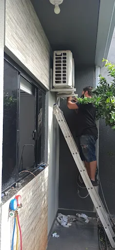 Técnico em escada instalando a condensadora do ar-condicionado na área externa de um apartamento